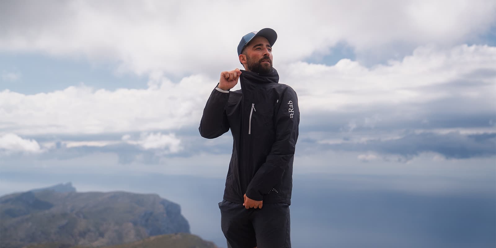 person wearing the RAB Downpour Trail light jacket on a mountain in Mallorca with dark clouds behind him